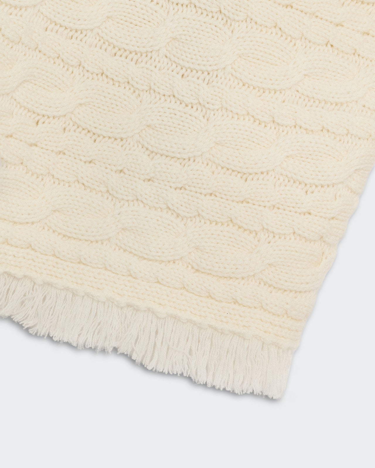 Close-up of cream Cropped Cable Turtleneck showing horizontal cable knit and fringe detailing at bottom hem.