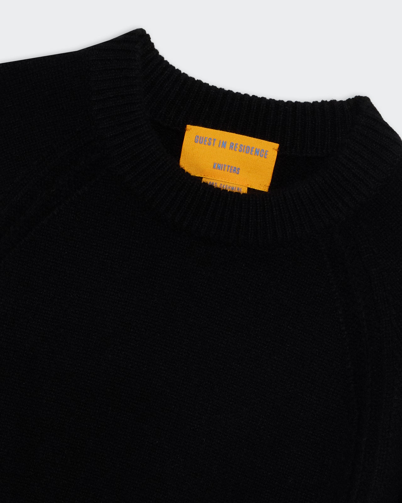 Close-up of black Sculpted Crew - Black cashmere sweater neckline with ribbed collar and orange branded label.