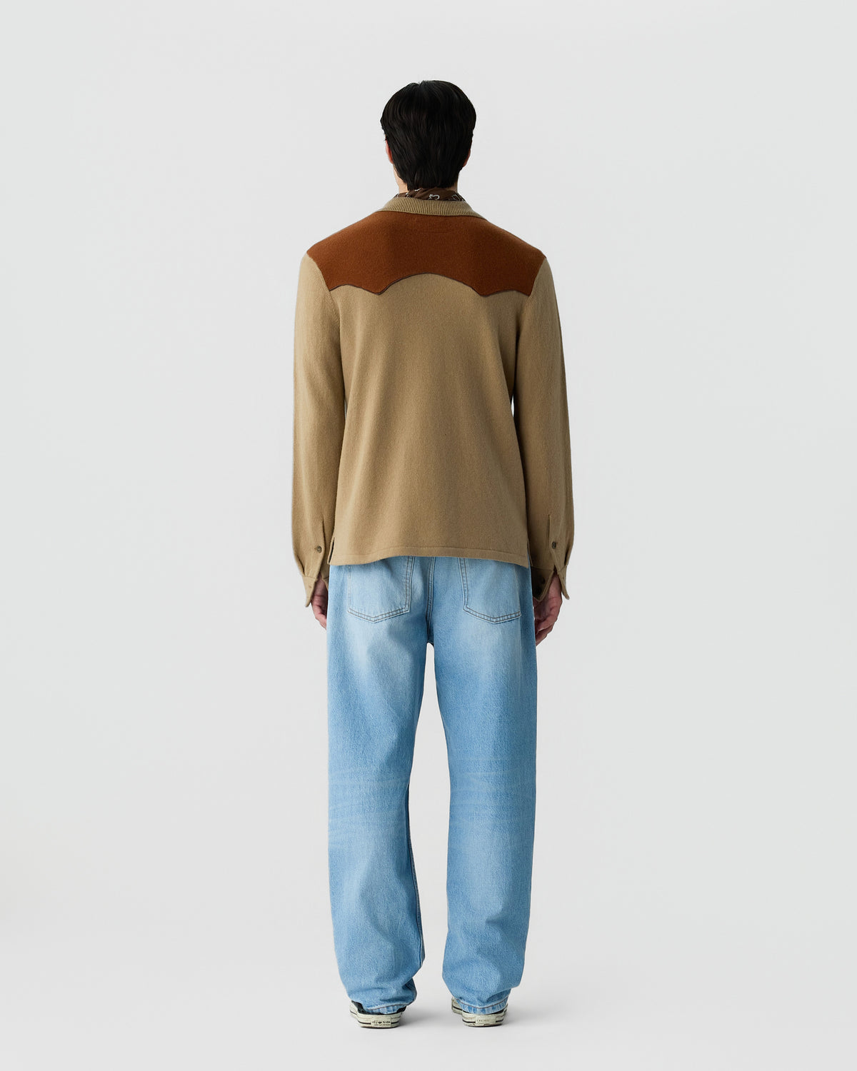 Man wearing a two-tone brown long-sleeve shirt with a yoke detail on the back, paired with light blue relaxed-fit jeans, standing against a plain white background.