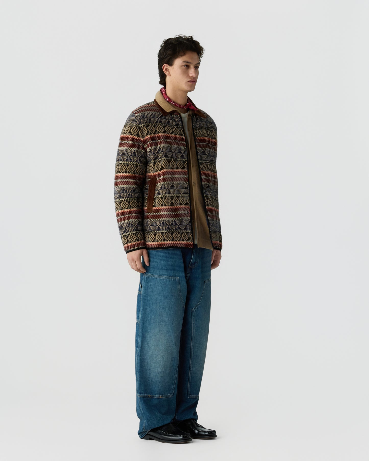 Model wearing a patterned knit cardigan with blue jeans and black shoes against a light gray studio background