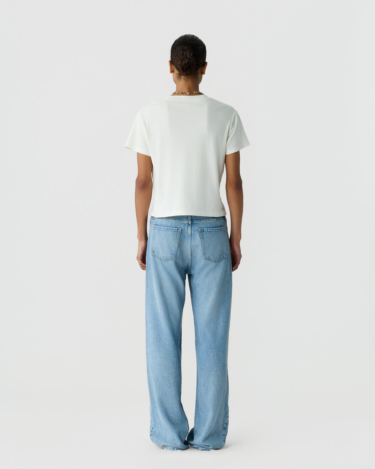 Back view of a person wearing a plain white short sleeve shirt and relaxed fit light blue jeans against a light gray studio background