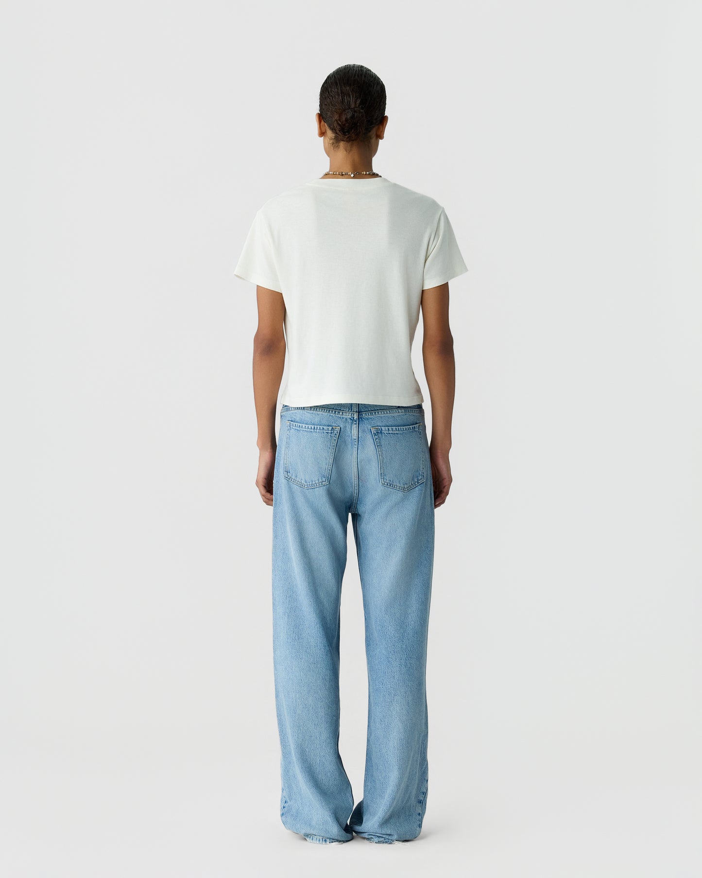 Back view of a person wearing a plain white short sleeve shirt and relaxed fit light blue jeans against a light gray studio background